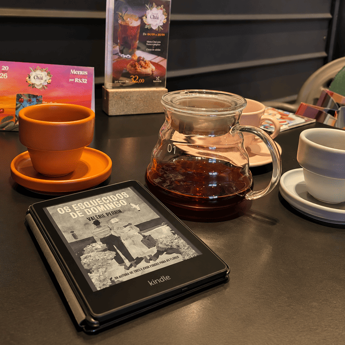A Kindle displaying Forgotten on Sunday by Valérie Perrin on a café table beside a cup of tea and a glass coffee maker.